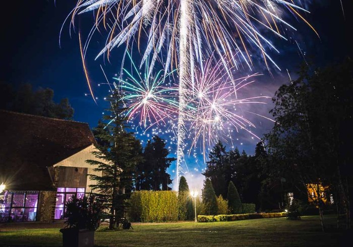 Feux d'artifice illuminant le ciel au-dessus du Domaine de Vaujoly, avec des arbres et un bâtiment en arrière-plan.