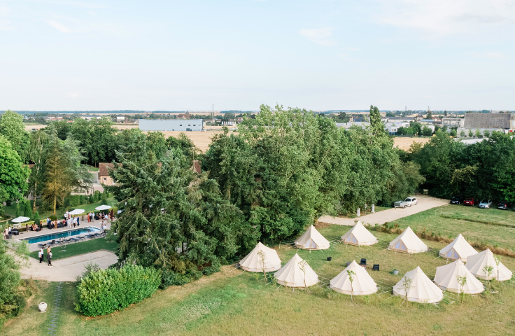 Vue aérienne du Domaine de Vaujoly, montrant une piscine entourée de verdure et des tentes de réception, symbolisant un lieu d'événements en plein air.